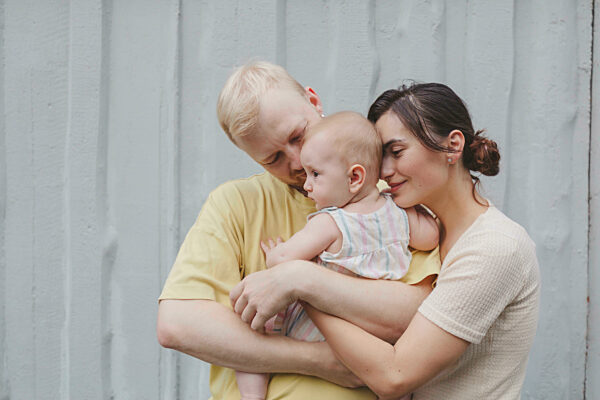 Mother and father embracing daughter in front of wall