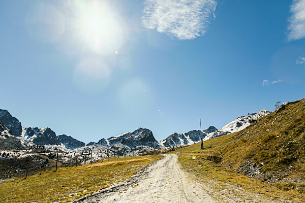 Dirt road leading towards snowcapped mountains on sunny day