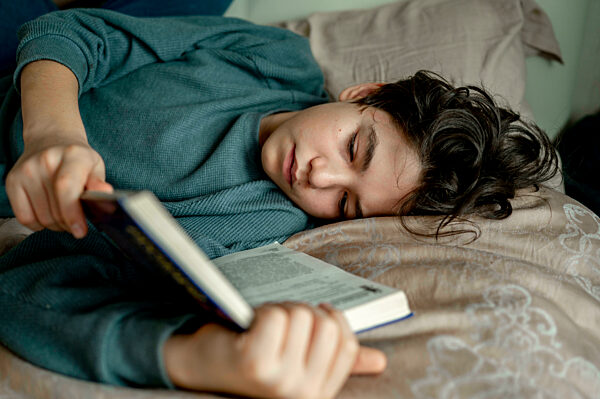 Boy reading novel lying on bed at home