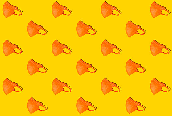 Pattern of rows of orange colored FFP2 masks flat laid against yellow background