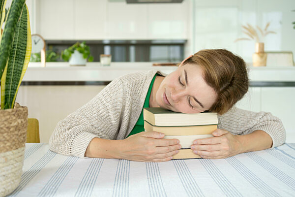Woman resting on stack of books at home