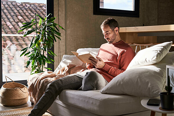 Man sitting on sofa reading book at home