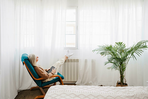 Thoughtful woman with book sitting on armchair at home