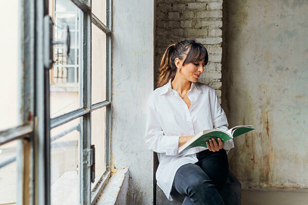 Woman reading book sitting by window