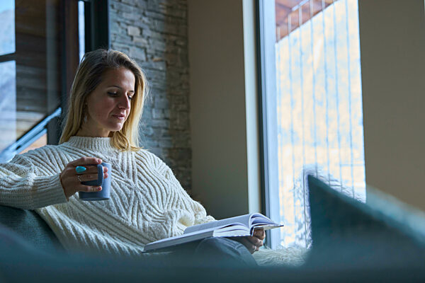 Woman reading book having coffee at home