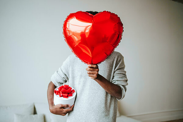 Man covering face with heart shape balloon at home