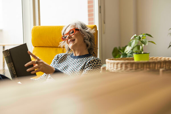 Smiling mature woman reading book sitting in armchair at home