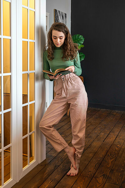 Young woman reading book leaning by door at home