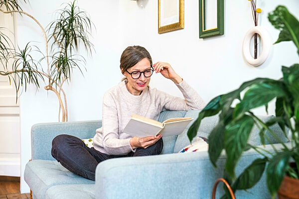 Mature woman wearing eyeglasses reading book