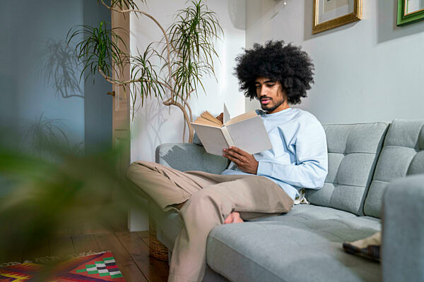 Man reading book sitting on sofa at home