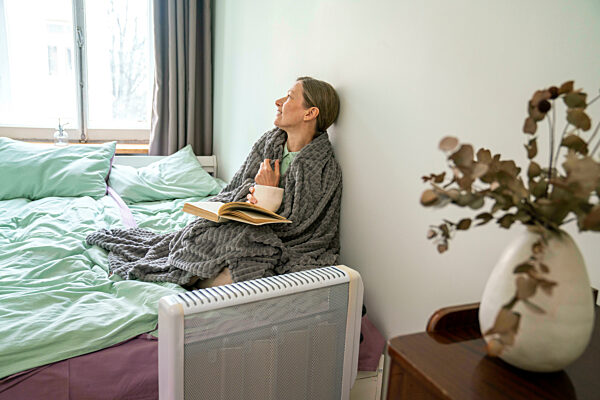 Thoughtful woman with blanket sitting on bed at home