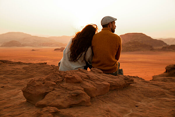 Couple sitting together on rock looking at desert at sunset
