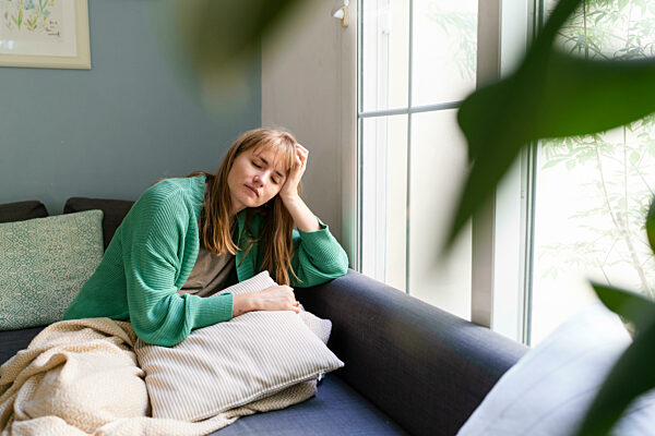 Sad woman with head in hands sitting on sofa at home