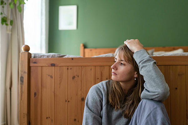 Contemplative woman with hand in hair sitting near bed at home