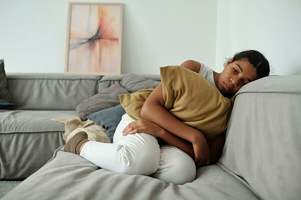 Depressed girl holding cushion and sitting on sofa at home