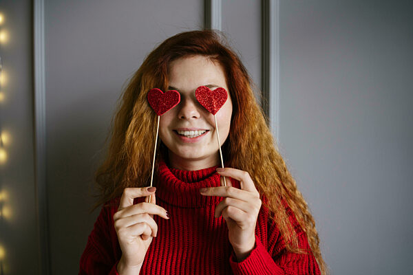 Playful woman holding heart shaped props over eyes at home