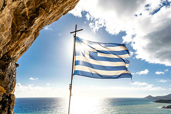Greece, Crete, Greek flag fluttering against sun shining over Mediterranean Sea