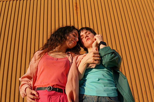 Gay couple standing with eyes closed in front of brown building wall