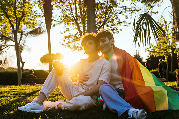 Young gay couple sitting together on grass at park