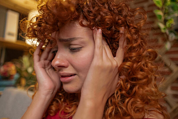 Stressed redhead woman touching temples at home