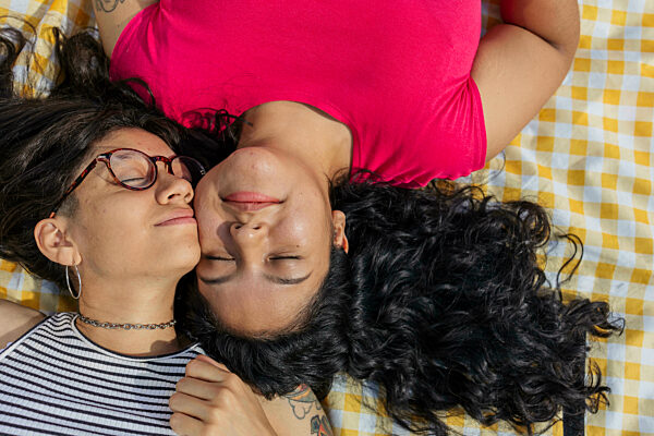 Young gay couple lying cheek to cheek on picnic blanket