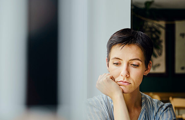 Sad woman leaning on elbow next to window at home