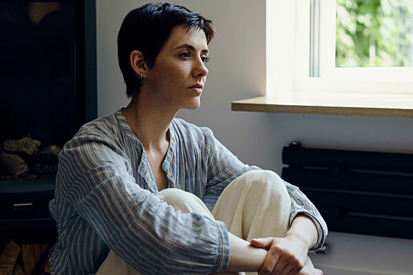Sad young woman hugging knees and sitting at home