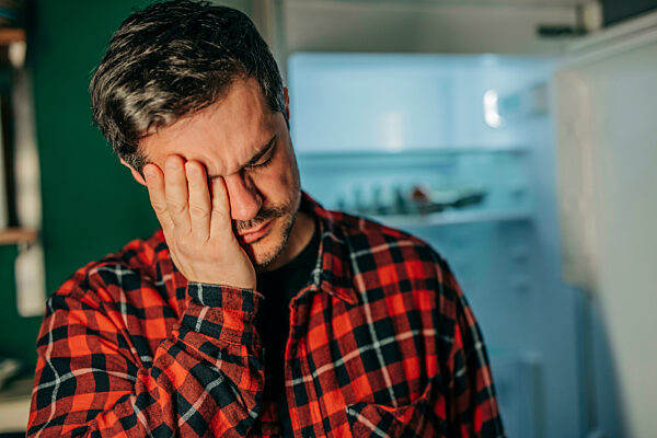 Sad man in plaid shirt covering face with hand at home