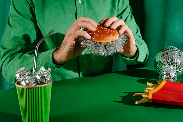 Man holding a hamburger filled with New Year's tinsel near fires kept on table