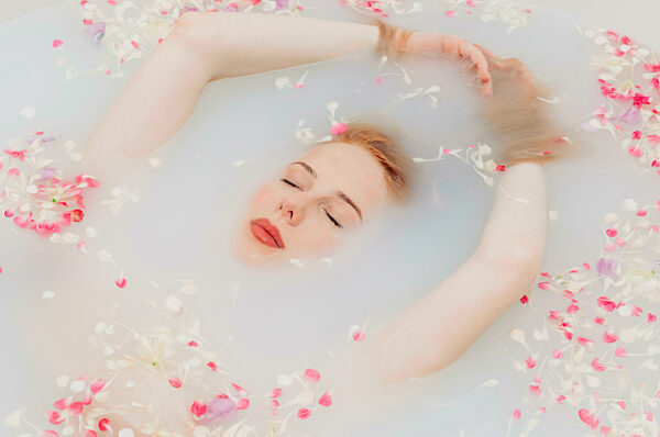 Woman with arms raised relaxing in water with flower petals