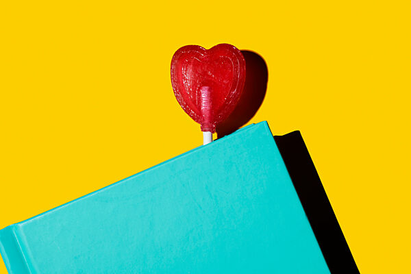 Heart-shaped lollipop on a turquoise book against a yellow background