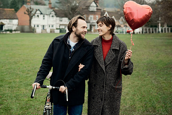 Couple walking in a London park with a heart-shaped balloon and a bike