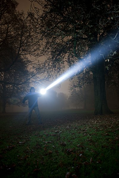 Germany, Munich, Man lighting spooky tree with torch in foggy night