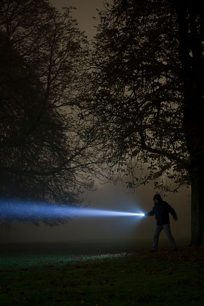 Germany, Munich, Man lighting spooky tree with torch in foggy night