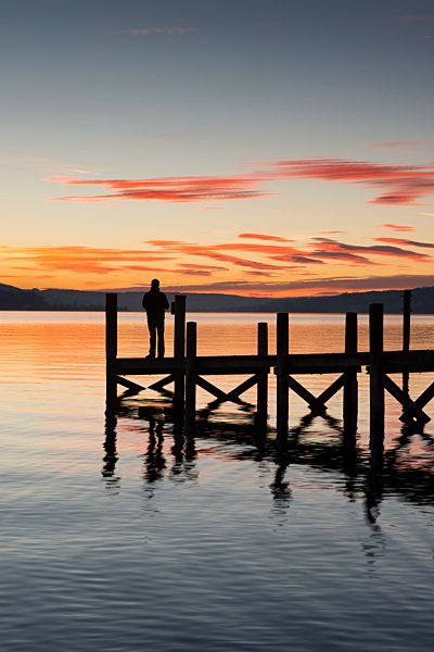 Germany, Baden Wuerttemberg, Person standing on pier at Lake Constance at dusk