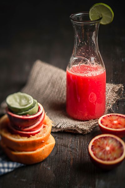 Bottle of juice with blood oranges on table, close up