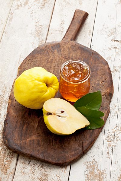 One and a half quince (Cydonia oblonga) and a glass of quince marmalade on wooden chopping board