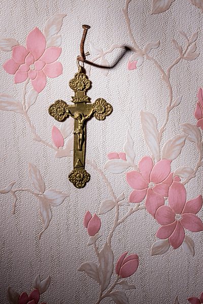 Crucifix hanging on bent nail in front of wallpaper with pink floral design