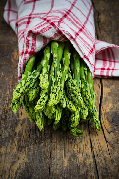 Bunch of green asparagus, Asparagus officinalis, wrapped in kitchen towel lying on dark wood