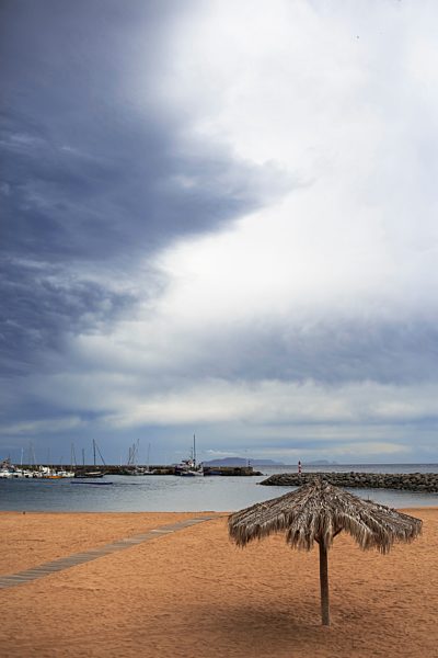 Portugal, Madeira, Machico, Yellow beach with beach umbrella, view to harbour