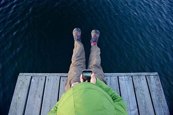 Sweden, Storuman, Man with cell phone sitting on jetty by the lakeside
