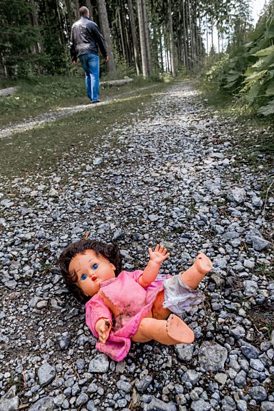 Austria, Linz, stripped doll lying on forest track while man going away