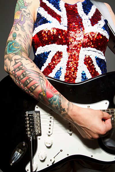 Close up of young woman playing guitar and tattoo on her hand against grey background
