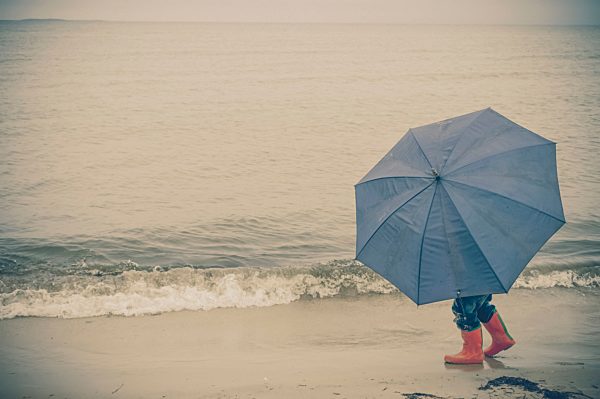 Germany, Mecklenburg Western Pomerania, Boy with umbrella in rain at baltic sea