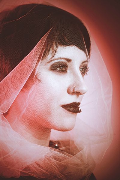 Portrait of young woman with veil and piercings in front of red background