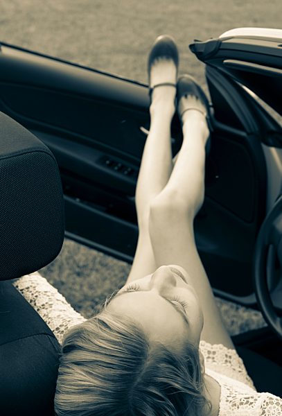 Young woman sitting in cabriolet with feet up, elevated view