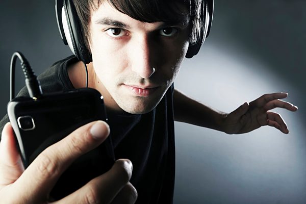Germany, Cologne, Young man with headphones listening music from smart phone