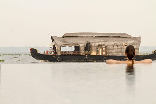 India, Kerala, Young woman in swimming pool looking at houseboat