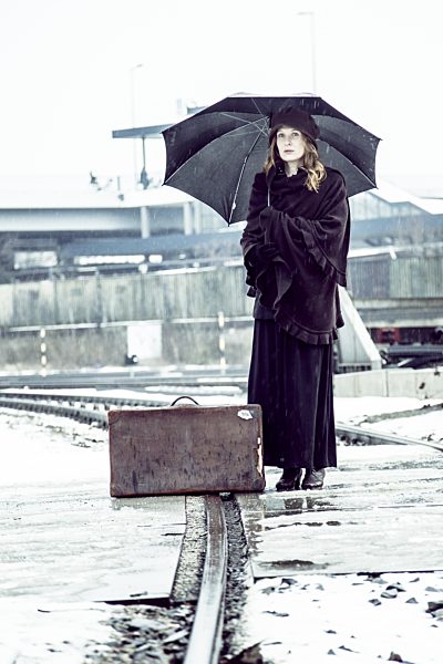 Germany, Berlin, woman with umbrella and old suitcase waiting at platform in winter