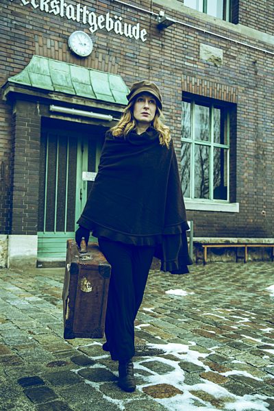 Germany, Berlin, woman carrying suitcase in front of old industrial building